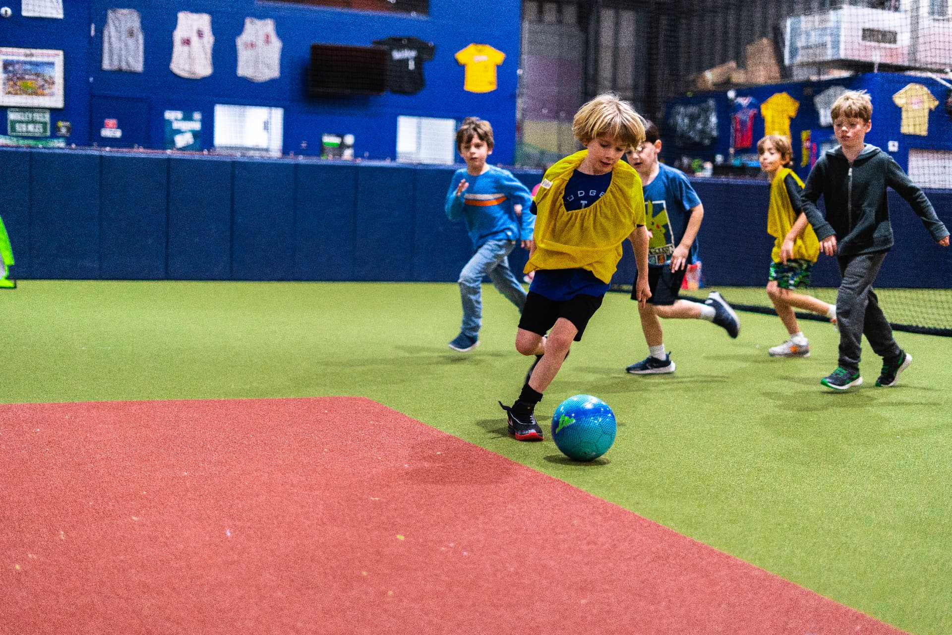 A camper dribbling a soccer ball past other kids during a camp game at JPLEX