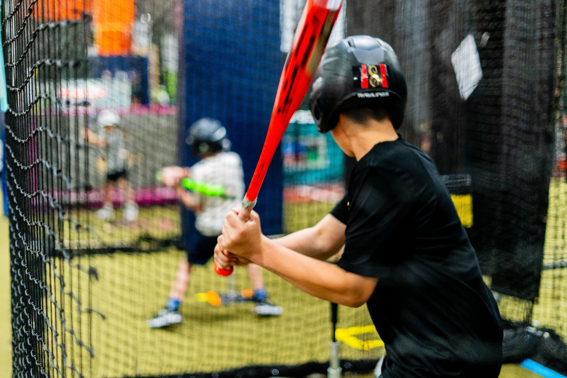 A player swinging inside a netted batting cage at Junction Place Sportsplex