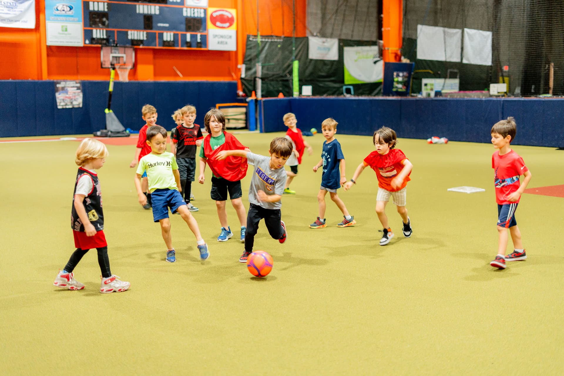 Wide view of the enclosed indoor turf field at Junction Place Sportsplex with a group of kids playing a field game